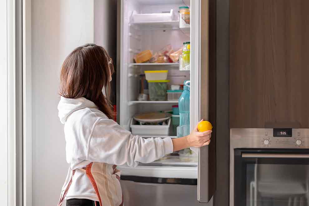 mulher na frente de uma geladeira pegando uma maçã em uma cozinha iluminada