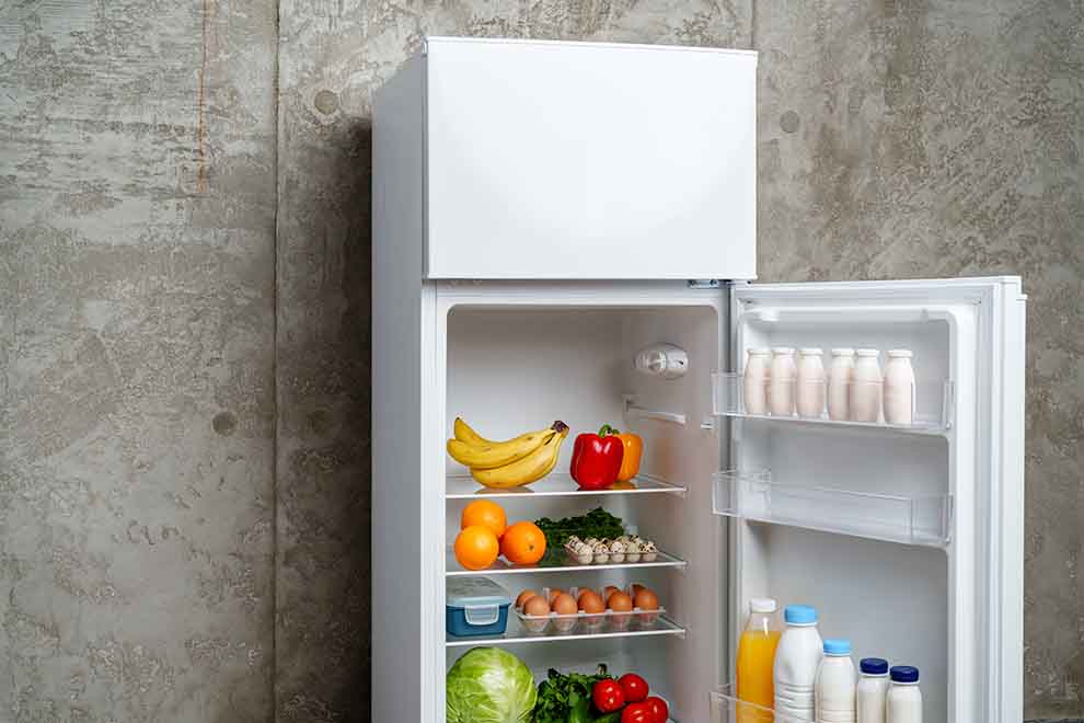 geladeira geladeira branca encostada em uma parede cinza com frutas e legumes dentro