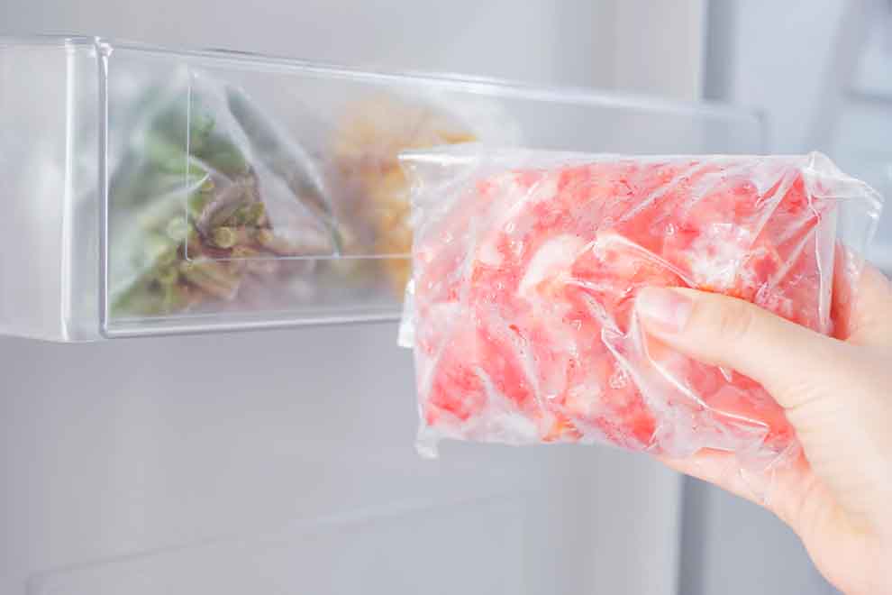 proteger alimentos durante o processo de desgelo pessoa retirando o alimento da geladeira ao descongelar em uma parede branca de uma cozinha