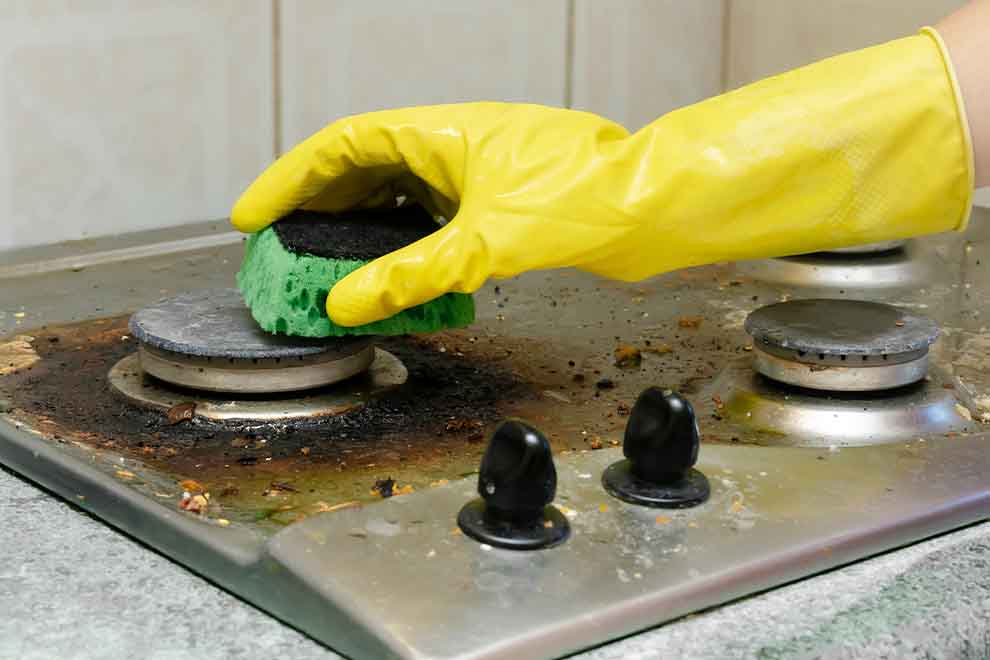 limpeza de fogão  pessoa limpando o fogão sujo em uma cozinha com uma luva de borracha