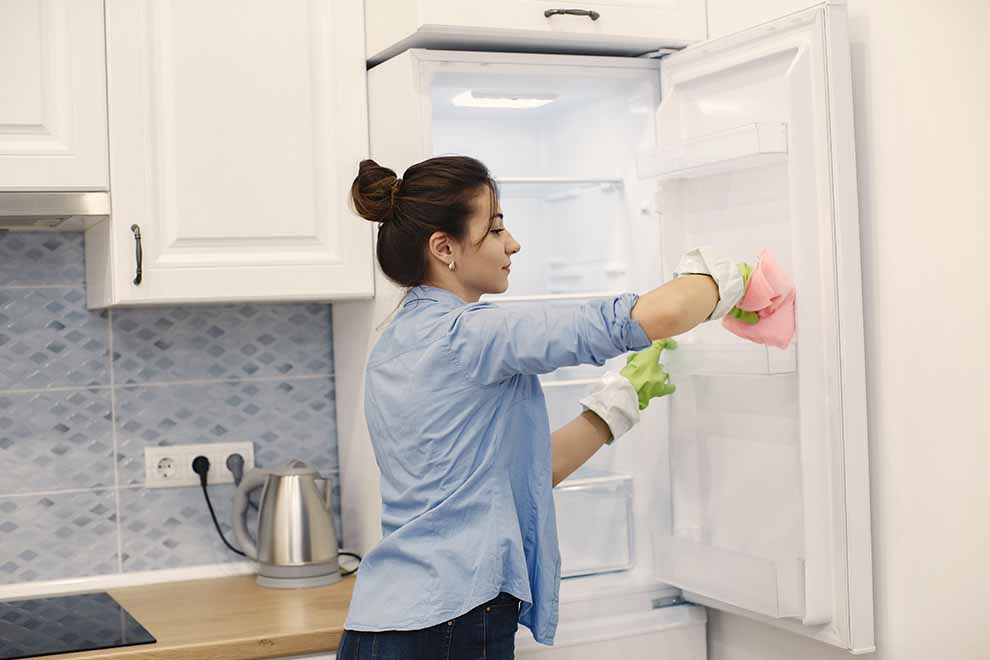 Mulher limpando a geladeira na cozinha