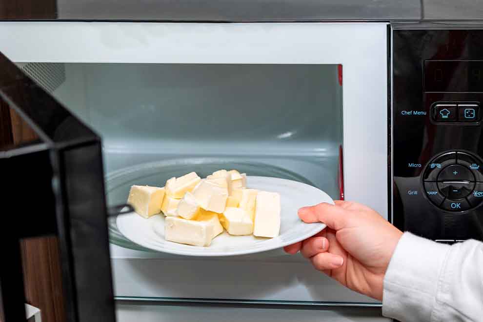 derreter mantega pessoa derretendo manteiga no microondas em uma cozinha branca