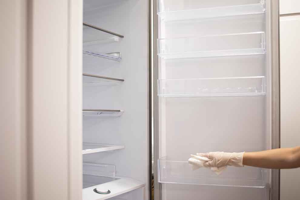 Pessoa limpando prateleira de geladeira vazia
