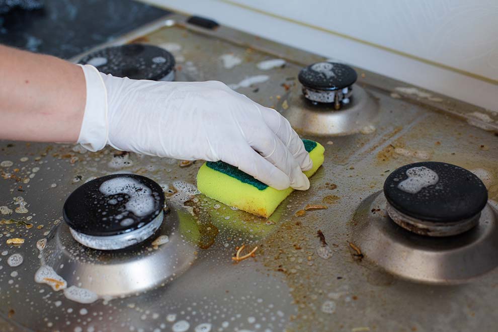 Mão limpando fogão sujo com esponja.